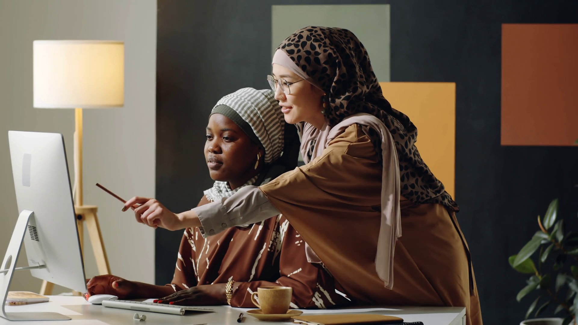 Medium long of young Muslim Black woman wearing hijab sitting at desk ...
