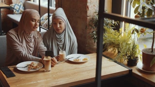 Two friends in hijabs enjoying coffee and browsing the Internet in a cafe
