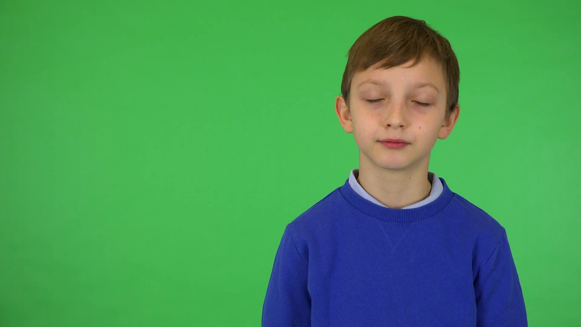A young cute boy nods at the camera with a smile green screen studio