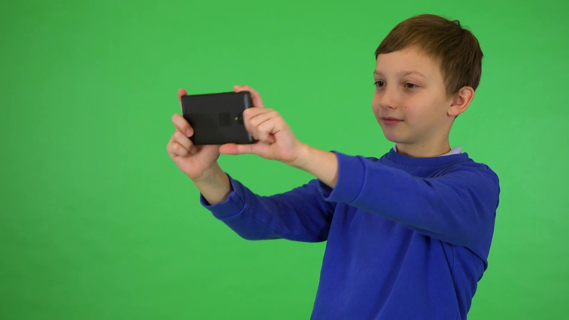 A young cute boy takes pictures with a smartphone green screen studio
