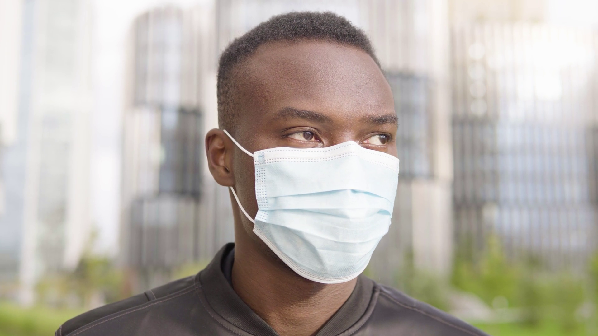 A young black man in a face mask looks around face closeup office