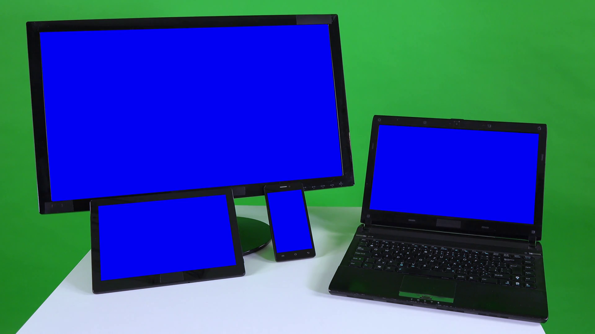 Various devices with blue screens on a white table against the green