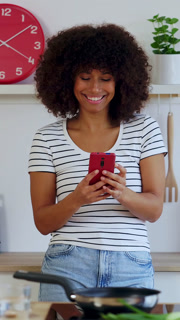 Young happy multiracial woman using mobile phone while cooking in the kitchen