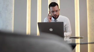 Professional businessman using laptop for a video conference call and smiling while working remotely in a modern office