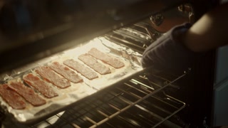 Handheld shot of black woman taking out baked bacon from oven