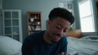 Handheld shot of African American man reading bible laughing lying on bed at home