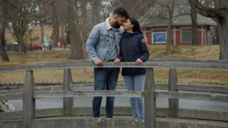 Full shot of Biracial couple embracing on the bridge creating their love story