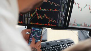 Man showing information on smartphone. Male and female stockbrokers in formal clothes works in the office with financial market and graphs on monitors