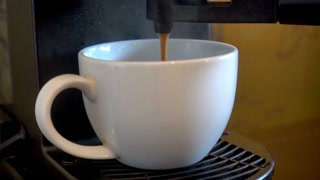 A white coffee cup sits beneath a coffee machine spout