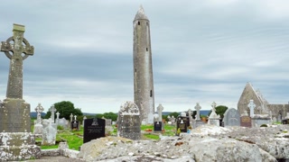 Irish graveyard with round tower and Celtic crosses under a cloudy sky scene