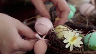 Hands decorating a colorful easter egg wreath with flowers and ribbon on a table