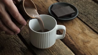 Cocoa or hot chocolate pouring into mug on rustic wooden background