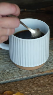 Vertical video. Female hand stirring sugar in cup and drinking black coffee