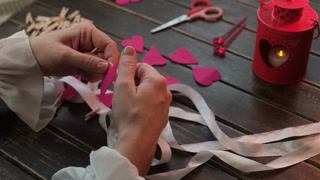 Hands making garland for St. Valentine's day. DIY home decoration. Felt hearts are pinned to white ribbon with clothespin.