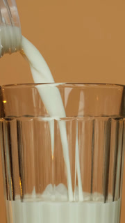 Vertical shot. Pouring milk into a transparent glass, close up