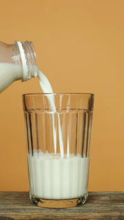 Vertical shot. Pouring milk into a transparent glass