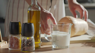 Woman placing cream in measuring cup on kitchen table during cooking