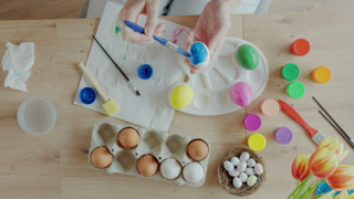 Woman painting Easter egg at home with pastel paints