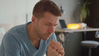Worried man sitting at home with clasped hands