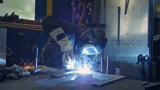 Seasoned skilled blue-collar worker working in a workshop creating sparks while welding metal materials, medium shot. Industrial concepts.