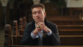Private moment of prayer, a man sitting on a wooden pew in a peaceful, empty Christian church, praying with rosary beads.