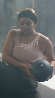 Vertical video: Gripping med ball, rotating lady in pink tank mirroring partner at gym, copy space