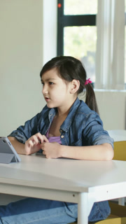 Vertical video: Following tablet lesson student tapping tablet and speaking at school desk in denim