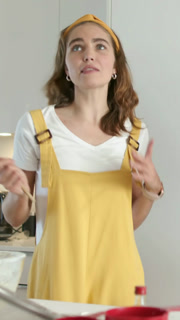 Vertical video: Holding wooden spoon to mouth, woman in yellow playing in kitchen touching bowl