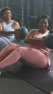 Vertical video: Cueing two women in blue and pink twisting passing medicine ball in gym for core