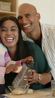 Vertical video: Holding grater woman while child grating cheese into bowl in kitchen couple kissing