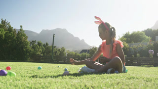 African American girl bunny-eared pink top spotting eggs, filling basket on lawn, copy space