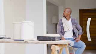 Man pausing from painting, scanning entryway, picking up ceramic mug and drinking by workbench