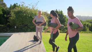 Senior woman leading mature female friends in sportswear heading to deck stepping up unrolling mats