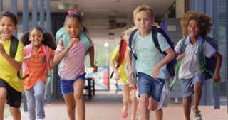 Front view of mixed-race schoolkids with schoolbags running in the corridor at school 4k