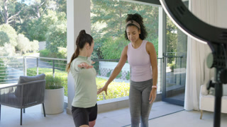 Female trainer guiding client assuming lunge on patio fixing form with pink band and ring light