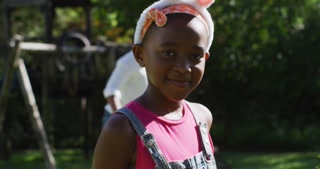 African american girl wearing easter bunny ears doing easter egg hunt in garden with brother