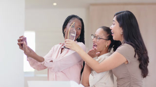 Diverse female friends, left woman raising purple phone, taking trophy selfie at lobby marking win