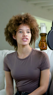 Vertical video: Recording host speaking into mic with pop on sofa at home for podcast, brown tee