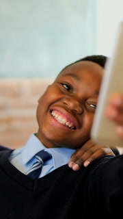 Vertical video: Reacting to peer hand on shoulder, boy in uniform posing for tablet selfie in class
