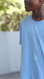 Vertical video: Panning cam man tee shorts turning head laughing by low white wall, copy space