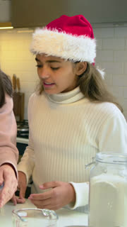 Vertical video: Starting holiday baking, family cracking eggs at kitchen counter, teen in Santa hat