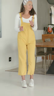 Vertical video: Entering mature woman in yellow overalls walking in dining, keeping beat near table