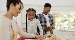 Happy african american parents and daughter unpacking shopping bag at home, slow motion