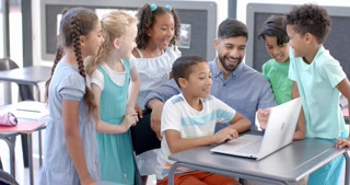 Young Asian man teaches in a school classroom, surrounded by diverse students