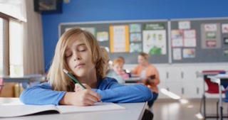 In school, boy holding pencil and resting head on desk in classroom