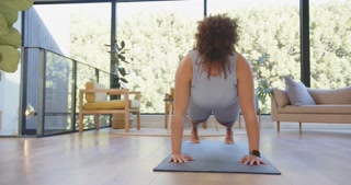 Exercising on yoga mat, plus size woman doing push-ups in modern living room