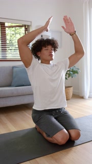 Vertical video: Practicing mindfulness, young man meditating on yoga mat in living room