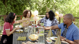 Group of happy multiracial, black and chinese male and female friends sitting at table and eating at
