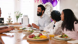 diverse family celebrating traditional ceremony, sitting at table, eating and embracing at home