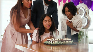 diverse family celebrating traditional ceremony, embracing and blowing candles at home with purple b